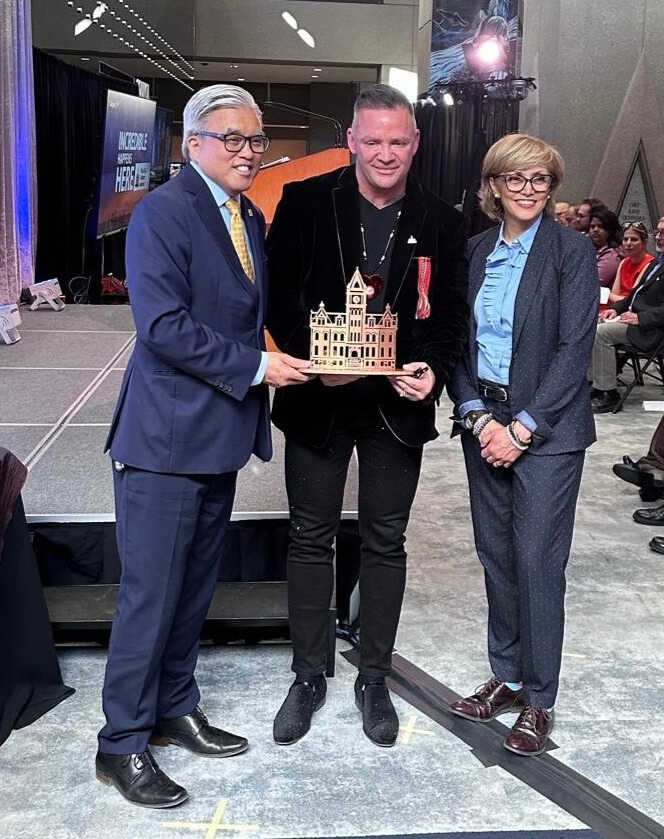 AFCC CEO Shane Gauthier stands on stage smiling, holding an award plaque, as Calgary Mayor Jyoti Gondek presents it to him during the 2024 Calgary Awards ceremony.